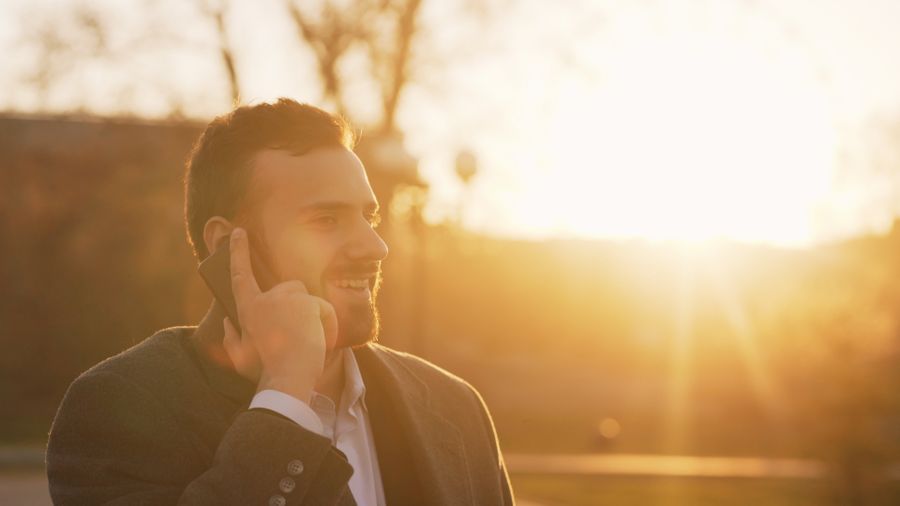 Person smiling while talking on the phone outdoors at sunset