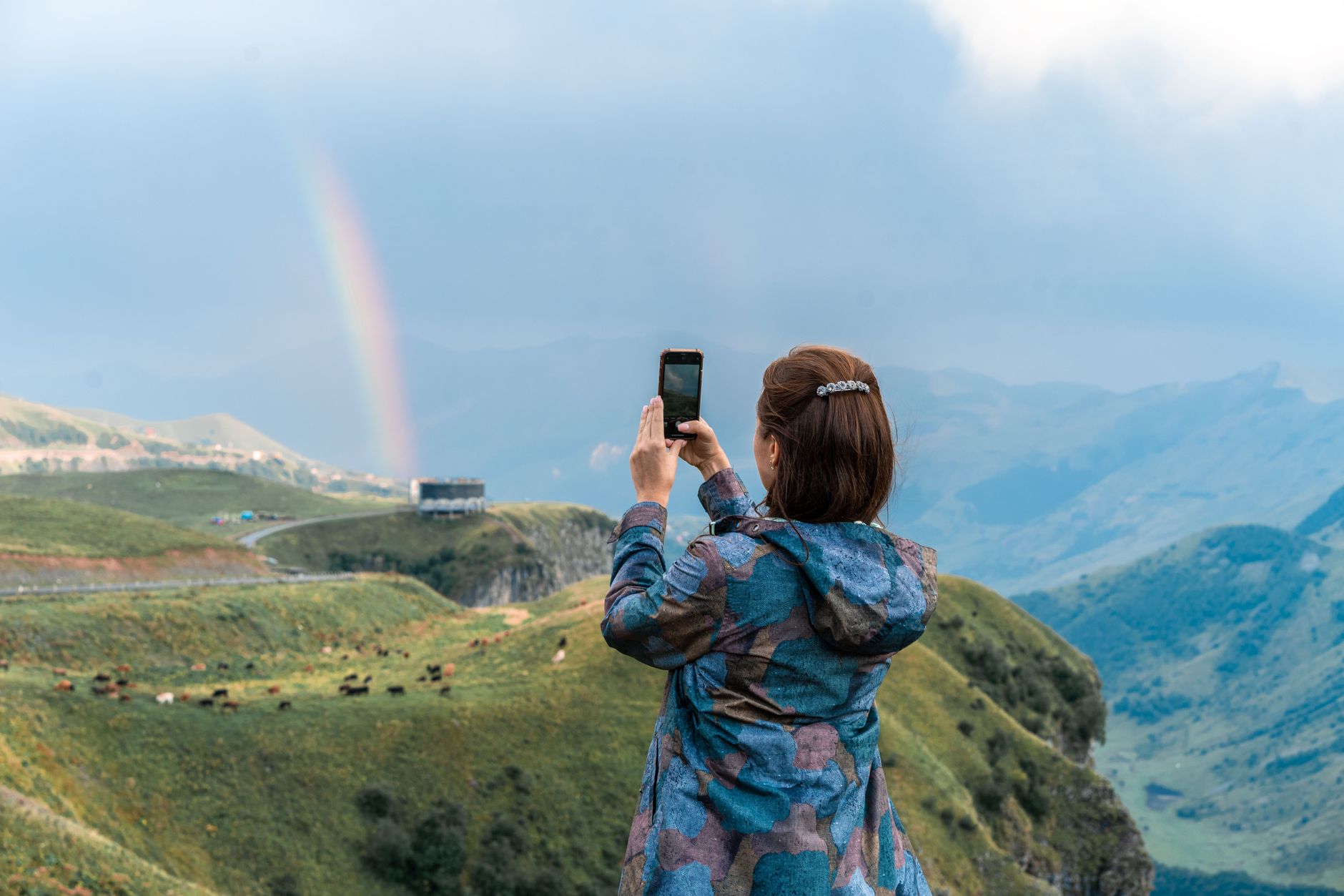 Traveler capturing a rainbow over the mountains with her phone